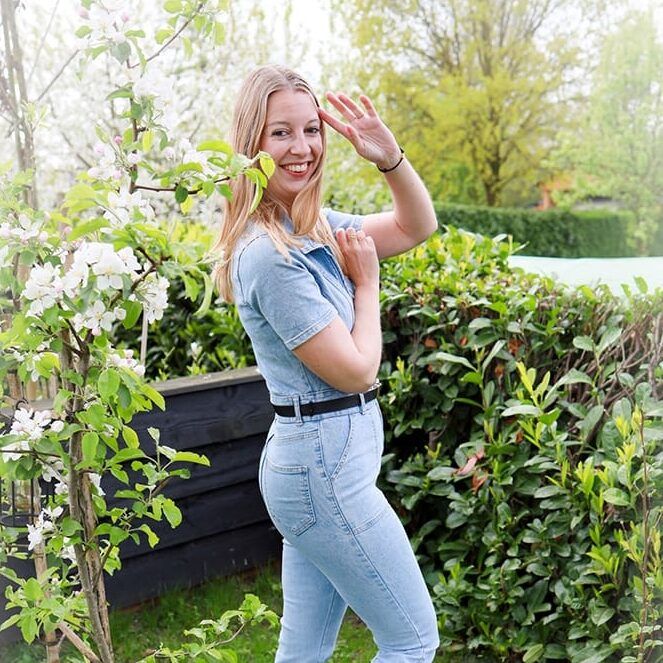 Lachende blondine in spijkerpak tussen de bloesem in de tuin, beeldmerk van girls-things.nl